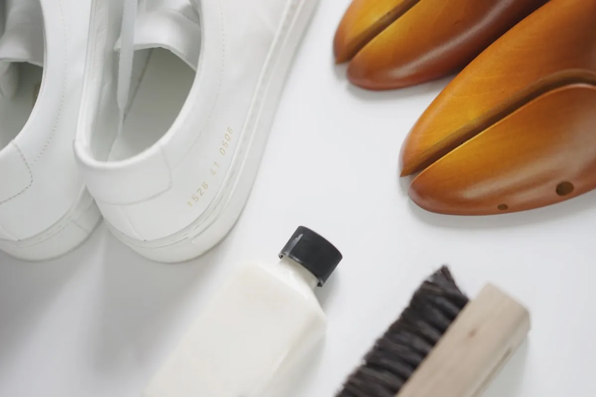 White trainers beside a shoe brush, cleaner and shoe trees